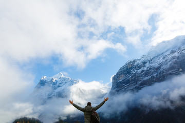 a man in the mountains in the clouds, man cheering elated and blissful with arms raised in the sky after hiking to mountain top summit above the clouds.