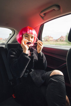 woman in a pink wig with sun glasses in hands in a car