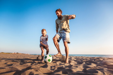 Happy father and son play soccer or football on the beach having great family time on summer holidays. - Powered by Adobe