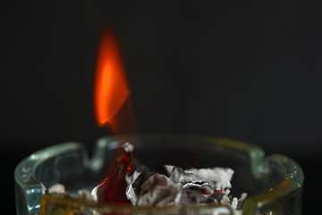A piece of paper burning in a glass ashtray close up