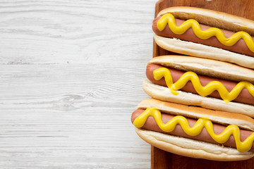 Hot dog with yellow mustard on wooden board on white wooden background, top view. Flat lay,...