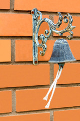 An ancient bronze bell with a rope on a red brick wall of a rich house.