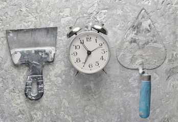 Building tools on a gray concrete background. Spatula, trowel, alarm clock, top view..