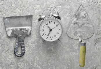 Building tools on a gray concrete background. Spatula, trowel, alarm clock, top view..