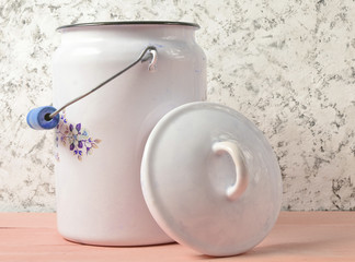 Enameled milk can with lid on white concrete wall background.