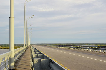 Road bridge over the river. Asphalt pavement, fences and lampposts, erased road markings. Cloudy weather. Copy space.