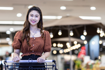 Beautiful Attractive Asian woman smile with shopping cart in supermarket feeling so happiness and enjoy,Shopping Concept