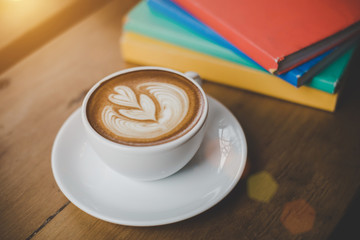 Close up hot coffee cup with book stacked on the table, warm tone.Cafe shop.