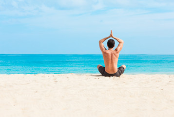 Fit male meditating on the beach. 