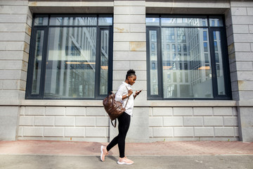 Full length portrait of a smiling african american woman with suitcase walking and talking on...