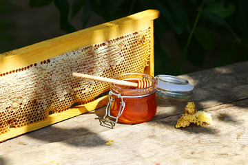 jar of fresh honey in a glass jar on an old table on a apiary. outside. frame with bees wax...