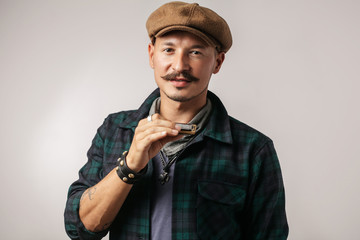 Rock musician in cap and whiskers playing a harmonica and looking at camera, Rock music and jam...
