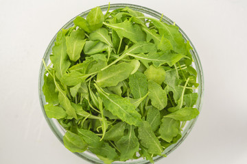 Fresh arugula salad in a glass bowl isolated on white background. Top view