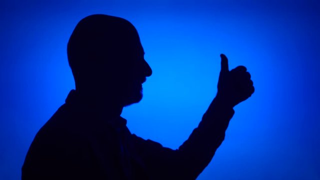 Silhouette of senior man making thumb up gesture on blue background. Male's face in profile showing thumbs-up sign. Black contur shadow of grandfather's half-face. Success and achievement concept