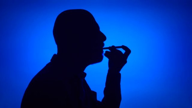 Silhouette of senior man using birthday whistle on blue background. Male's face in profile celebrating. Black contur shadow of grandfather's half-face. Celebration concept