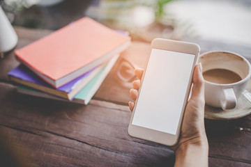 Mockup portrait of a woman hand holding a  cell phone with blank screen and a cup of coffee in cafe.
