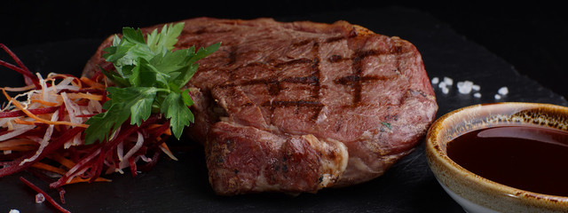 Roast beef barbecue with vegetables and sauce on a black background