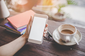 Mockup portrait of a woman hand holding a  cell phone with blank screen and a cup of coffee in cafe.