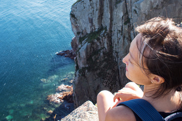Young woman sitting on edge of cliff, landscape. 