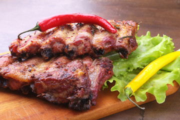 grilled barbecued ribs with lettuce leaves, hot chili pepper and sauce on wooden cutting board.