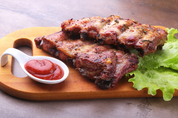 grilled barbecued ribs with lettuce leaves, hot chili pepper and sauce on wooden cutting board.