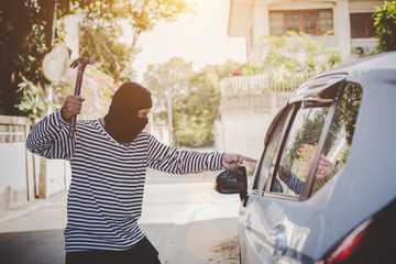 Thief wearing a black robe holding a hammer gunpoint robbery to steal a car.