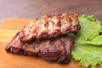 grilled barbecued ribs with lettuce leaves, hot chili pepper and sauce on wooden cutting board.