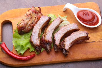 grilled barbecued ribs with lettuce leaves, hot chili pepper and sauce on wooden cutting board.