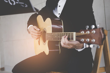 Close up musician sitting on chair acoustic guitar. Man wearing a suit  is playing guitar on a white background.