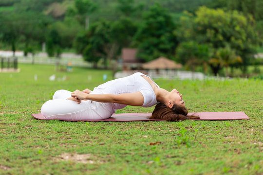 Beautiful Attractive Asian woman sitting on yoga mat practice Supta Virasana with yoga meditation relax and refresh health on green grass feeling happiness and comfortable in garden,Yoga Healthy Conce