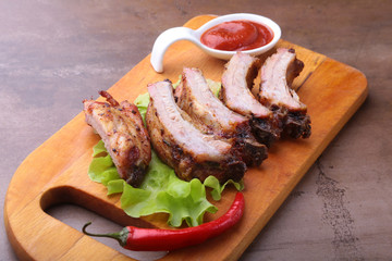 grilled barbecued ribs with lettuce leaves, hot chili pepper and sauce on wooden cutting board.