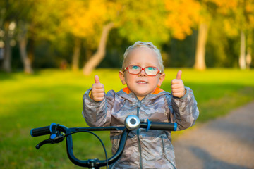 Счастливый улыбающийся мальчик в очках, на велосипеде осенью в парке 