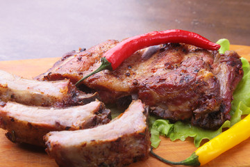 grilled barbecued ribs with lettuce leaves, hot chili pepper and sauce on wooden cutting board.