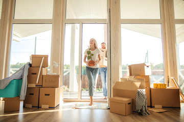 Happy smiling couple moving in new house and carrying carton boxes