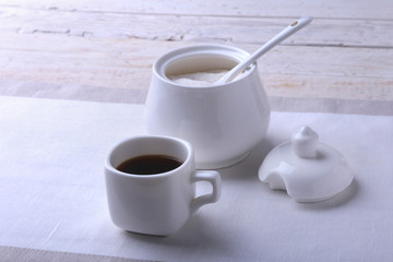 Cup of hot coffee espresso, coffee beans, jug of milk, and bowl with sugar on white background for copy space. Coffee concept.