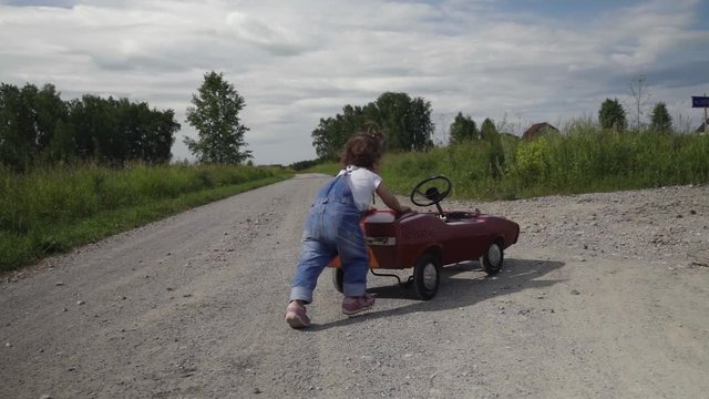 A little girl is pushing her big toy car along the road