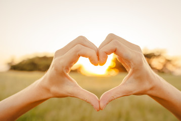 Hand shaped heart against beautiful sunset. 