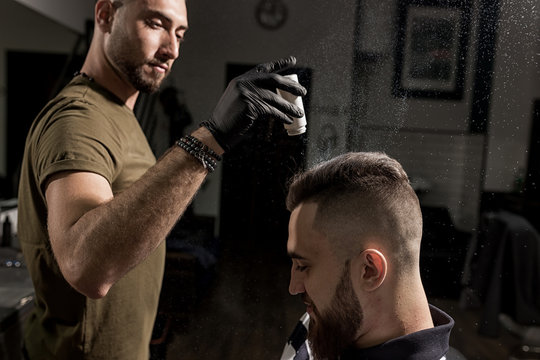 Handsome barber is fixing the styling of brutal young man with a dry styler at a barbershop