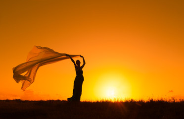 Pregnant woman holding a silk cloth blowing in the sunset. 
