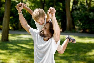 Father is playing with his little son. Father raised his little son on his right shoulder and smile. The boy is amazed.