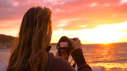 CLOSE UP: Unknown female photographer filming the sunset from a scenic beach.