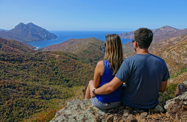 Naklejka na ściany i meble CLOSE UP: Unrecognizable couple sitting on rocky ledge overlooking the seaside.