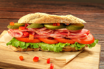Sandwich with tomatoes, ham salted cucumber on a wooden board