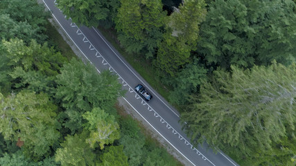 AERIAL: Flying above a dark car driving down empty road and through the forest.