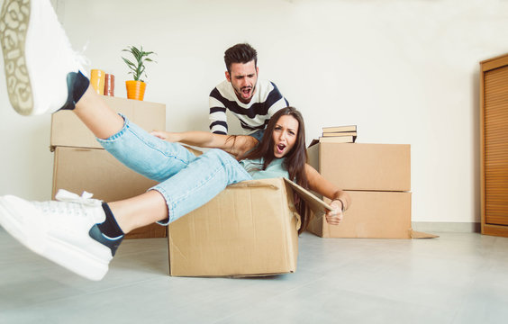 Happy couple is having fun with cardboard boxes in new house at moving day, 