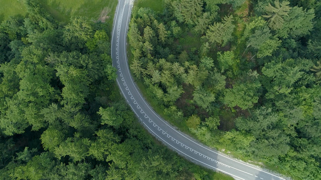 TOP DOWN: Flying above an empty asphalt road winding past forests and meadows. © helivideo
