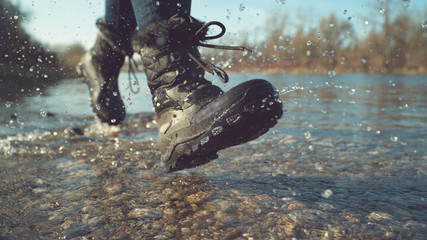 LOW ANGLE: Energetic young woman in fuzzy boots playing by the tranquil stream.