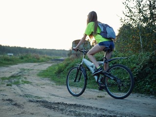 Fototapeta na wymiar Polonne / Ukraine - 14 September 2018: girl in a green T-shirt with a backpack riding a bike