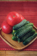 a fresh vegetable set of cucumbers and tomatoes on a bamboo plate. the view from the top. vertical