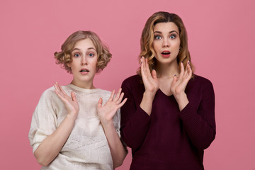 Beautiful sisters made a surprised face on a pink background.  The girls are shocked by the sale in the brand store.